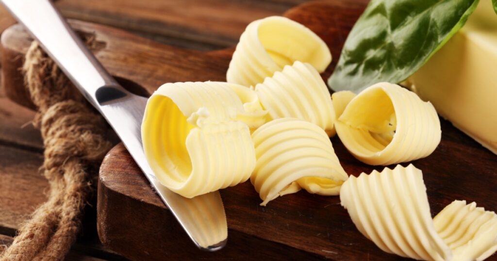 yellow block of fresh butter sliced on wooden cutting board and butter swirls. Slices of margarine or spread, fatty natural dairy product. High-calorie food for cooking