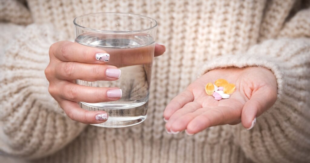 Woman hands holding glass of water, vitamins and supplements. B12, D3, selenium. Vitamins for vegans.