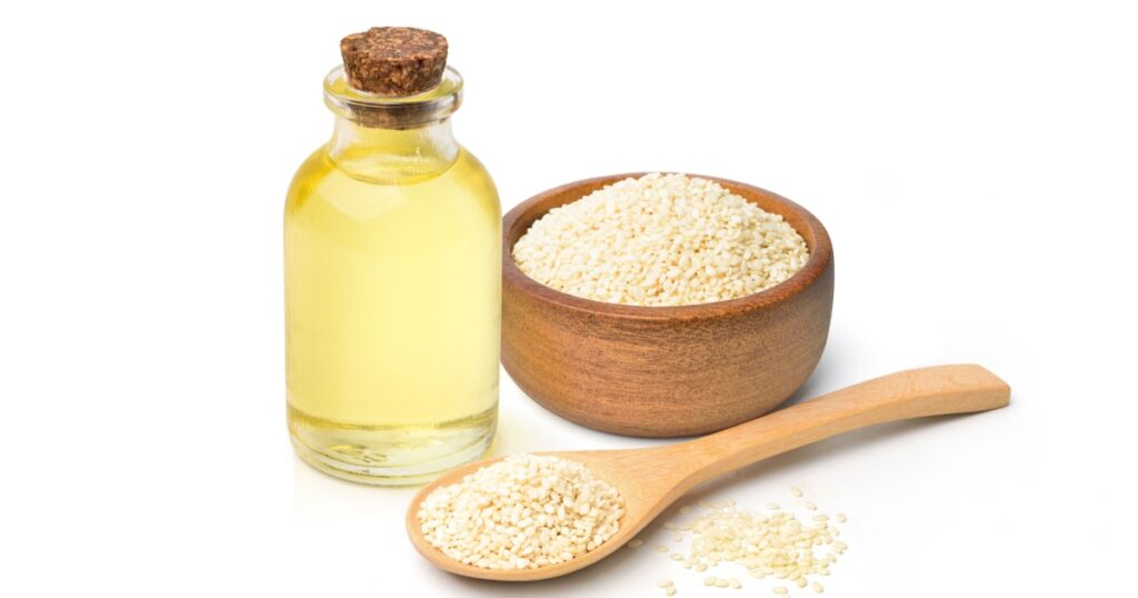 Sesame oil with white sesame seeds in wooden bowl and wooden spoon isolated on white background.