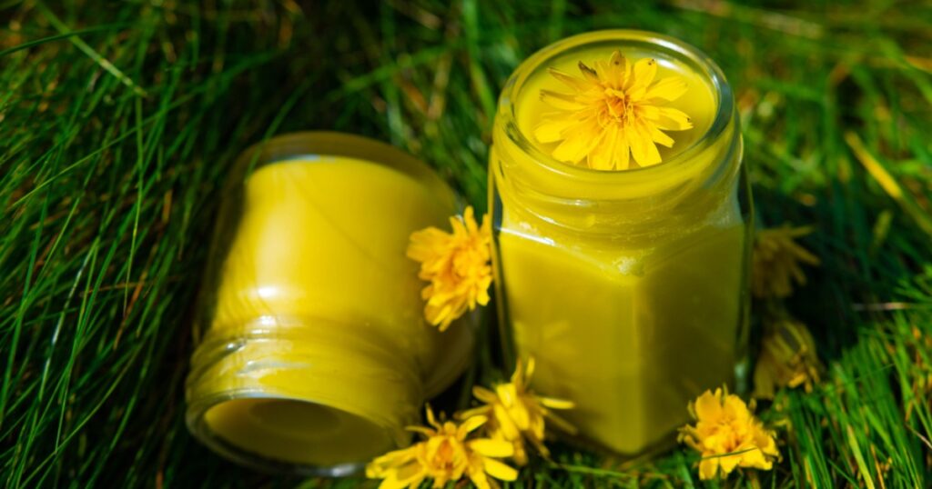 two yellow salve, creem, jars on a green grass with yellow flowers