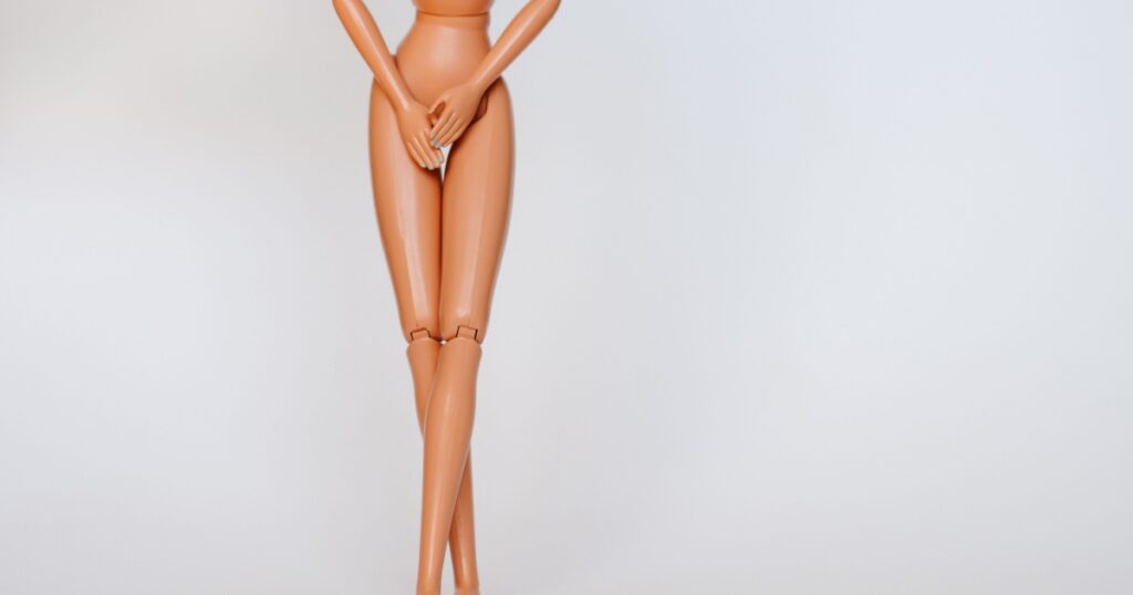 Nude doll covering pelvic area on white background. Female figure having UTI problems.