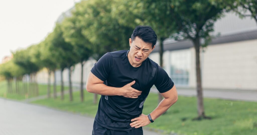 Male asian athlete, has chest pain fitness in the park and running, heart aches after cardio exercise