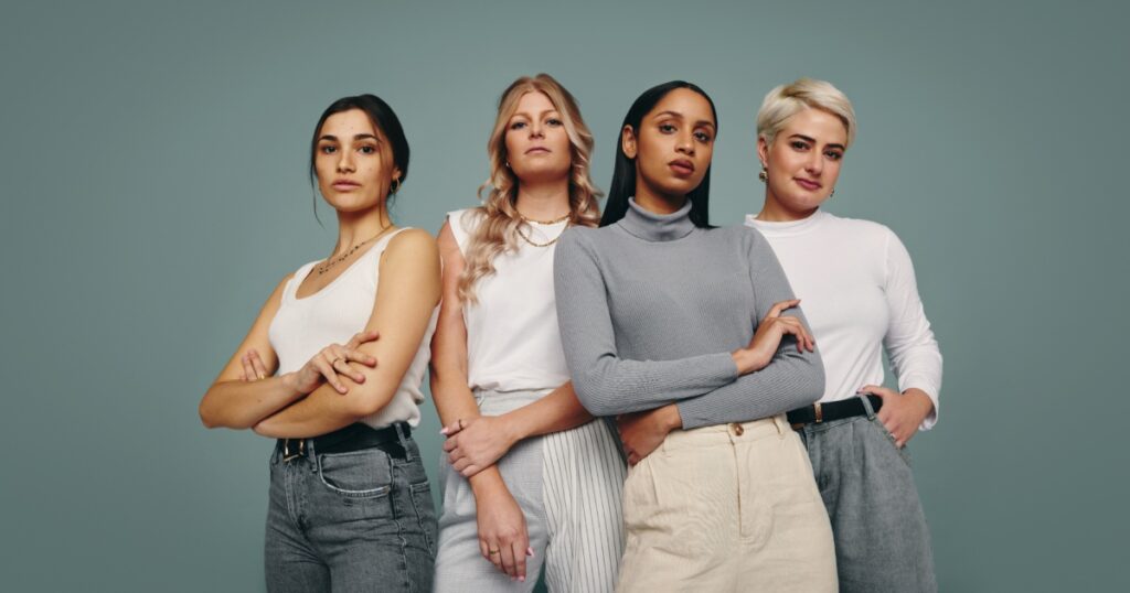 Group of fashionable women standing together in a studio. Diverse women looking at the camera while standing against a studio background. Four female friends looking confident in a studio.