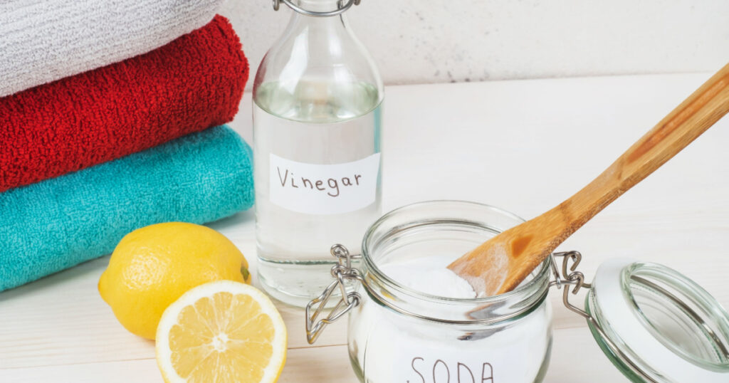 Baking soda in jar with a wooden spoon on top, vinegar, cut lemon, folded towel on a white background. The concept of organic removing stains on clothes. High quality photo