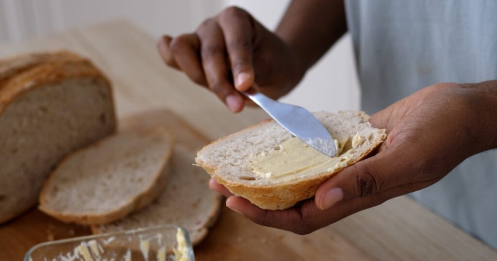 Smear organic butter on bread. Soft butter spreading on slice of sourdough bread. Carbohydrates, fat concept