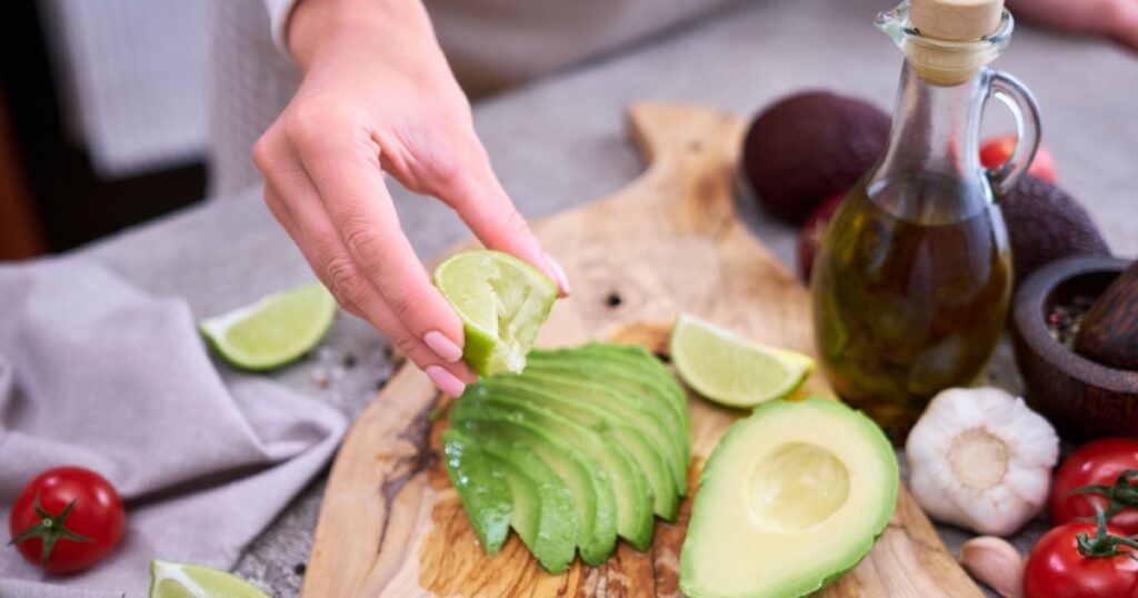 woman squeeze fresh lime juice onto Sliced avocado on wooden cutting board at domestic kitchen