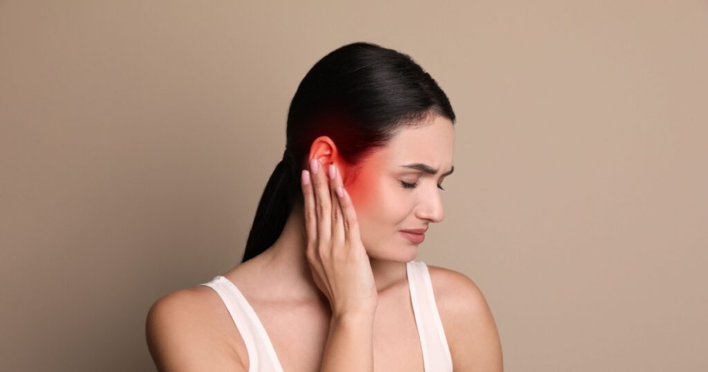 Woman suffering from ear pain on beige background