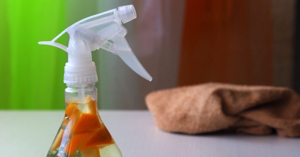 Flavored white vinegar with rosemary and orange zest in a clear spray bottle. Ecological detergent for cleaning the house. The concept of refusal to use harmful household chemicals.