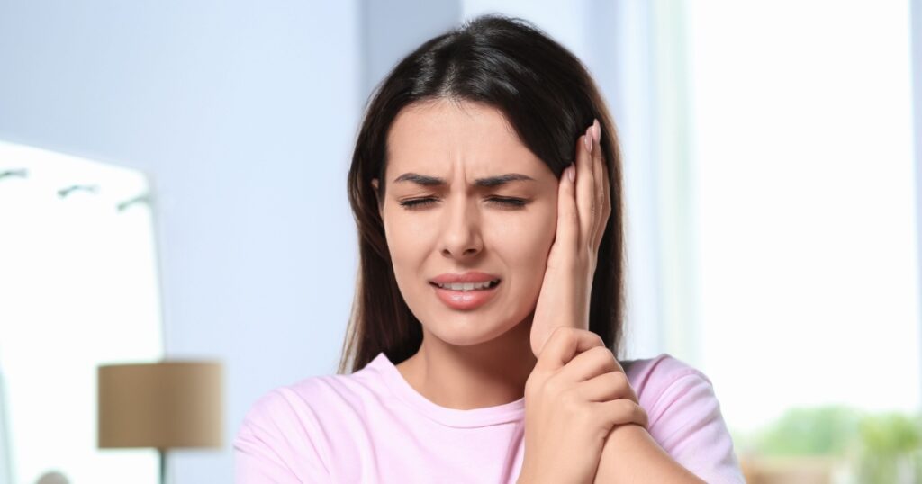 Young woman suffering from ear pain indoors