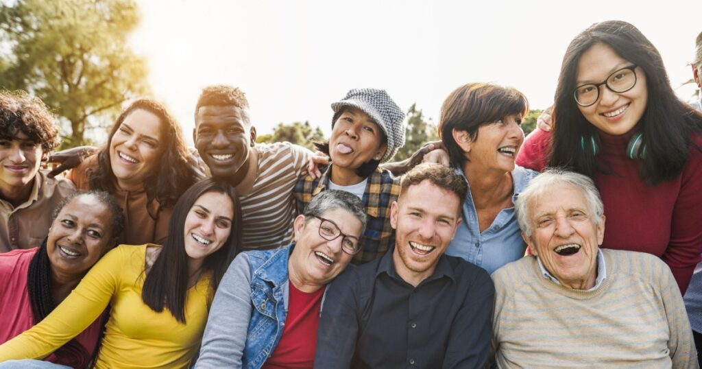 Group of multigenerational people smiling in front of camera - Multiracial friends of different ages having fun together - Main focus on caucasian senior faces