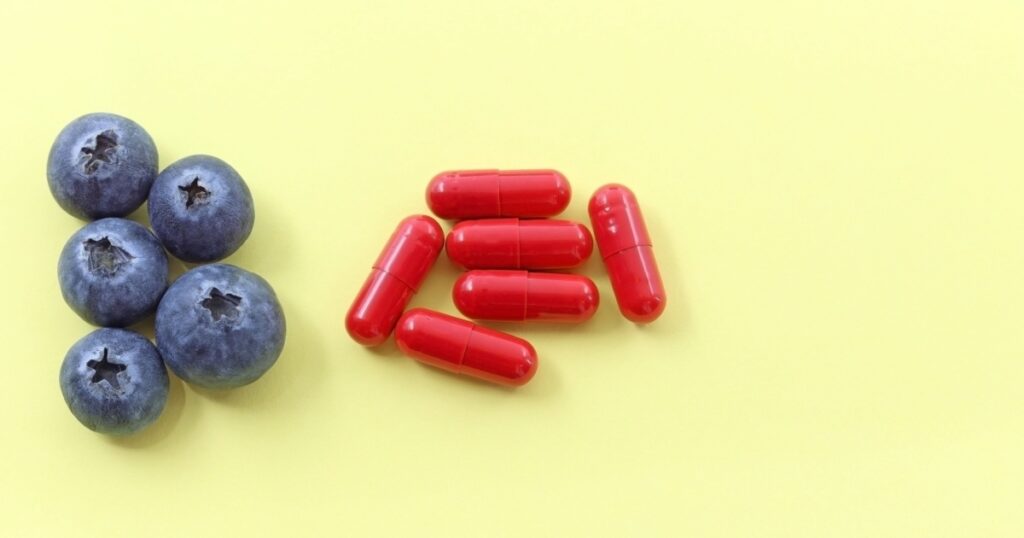 Some blueberries next to red capsules, pills, or UTI medications