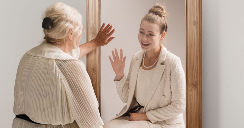 Creative conceptual collage. Tender image of senior woman looking in mirror and smiling to her young self reflection. Back to past. Concept of present, past and future, age, lifestyle, memories, ad