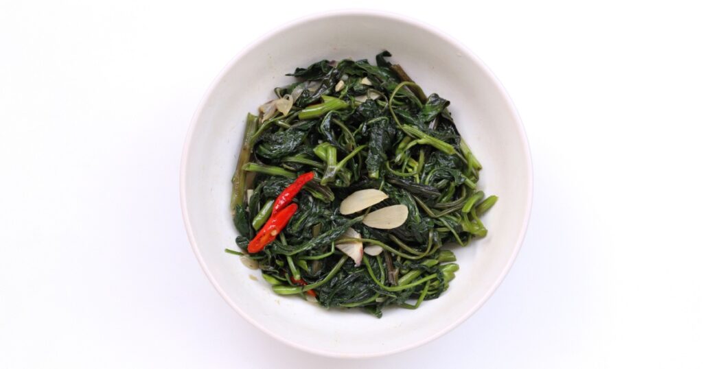 Indonesian traditional food named "tumis kangkung bawang putih" i.e. sauteed water spinach with garlic, served on plate isolated on white background, top view