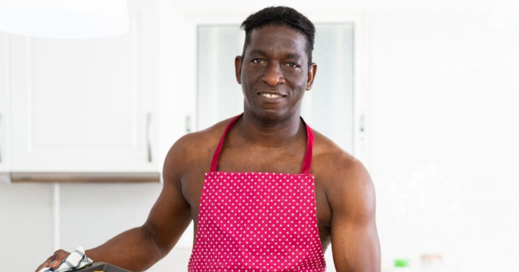 Cheerful naked man in red apron holding