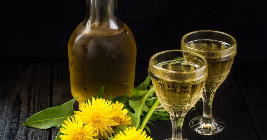 Cooled homemade dandelion wine in old wineglasses, bottle and wreath from dandelions on a dark background