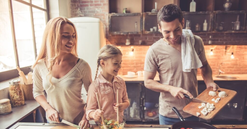 Cute little girl and her beautiful parents are smiling while cooking in kitchen at home