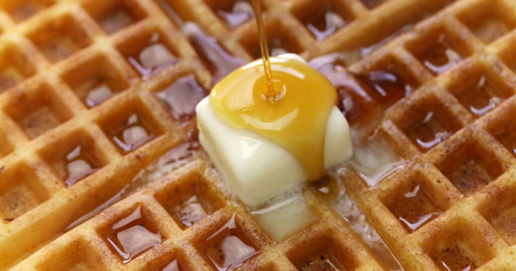pouring maple syrup over homemade american round waffles with butter