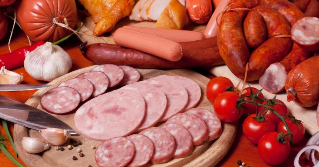 A variety of processed cold meat products, on a wooden cutting board.
