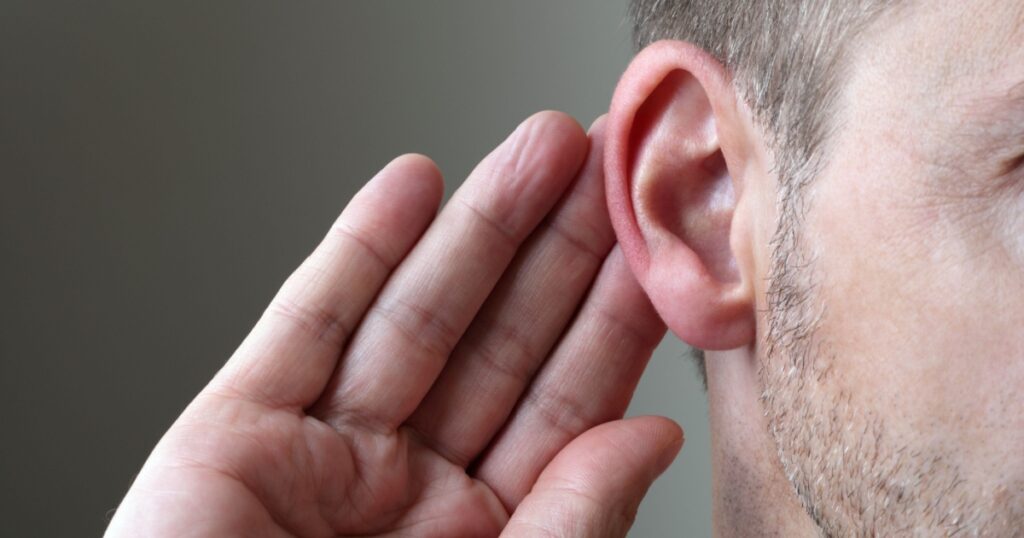 Close up on hand and ear listening for a quiet sound or paying attention