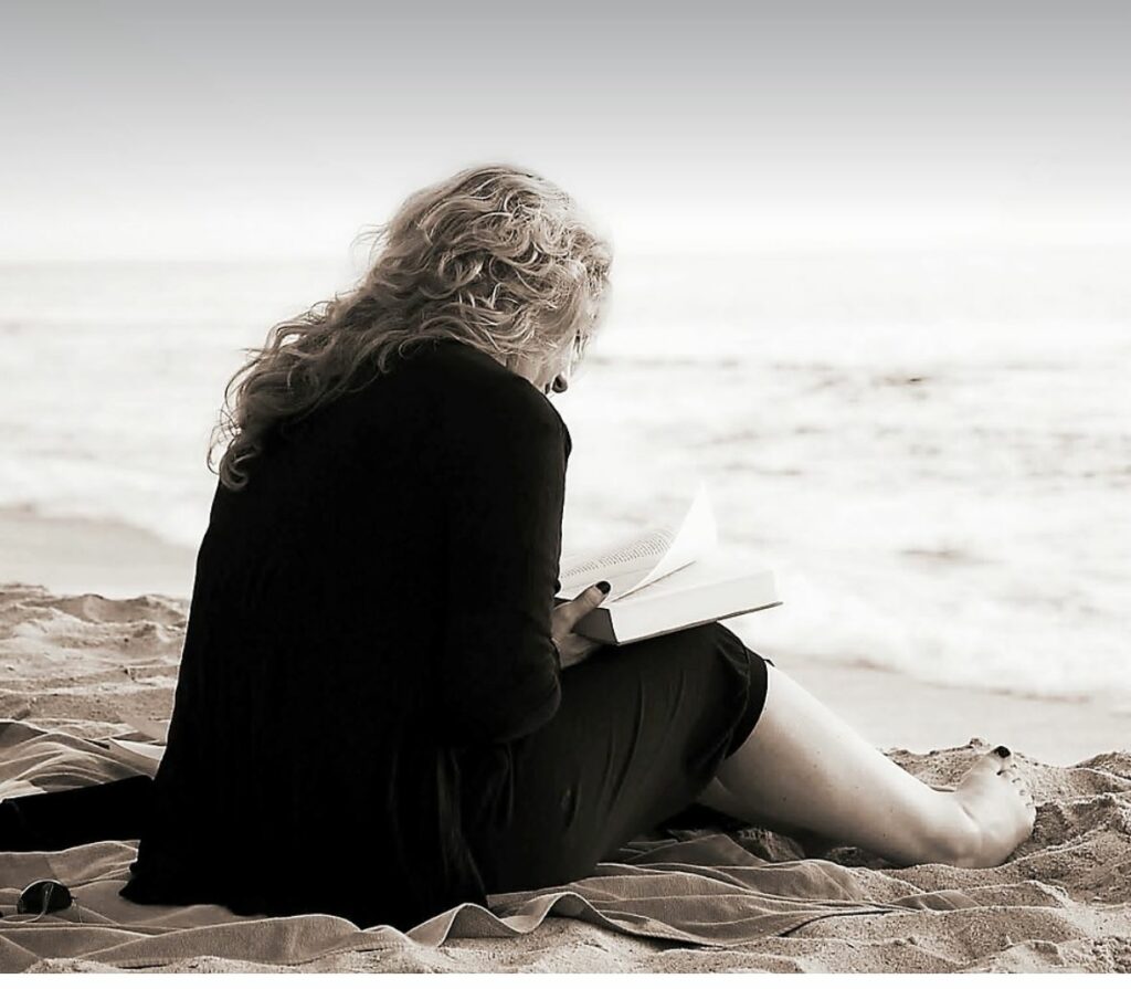 Black and white photo of a woman reading on the beach alone. 