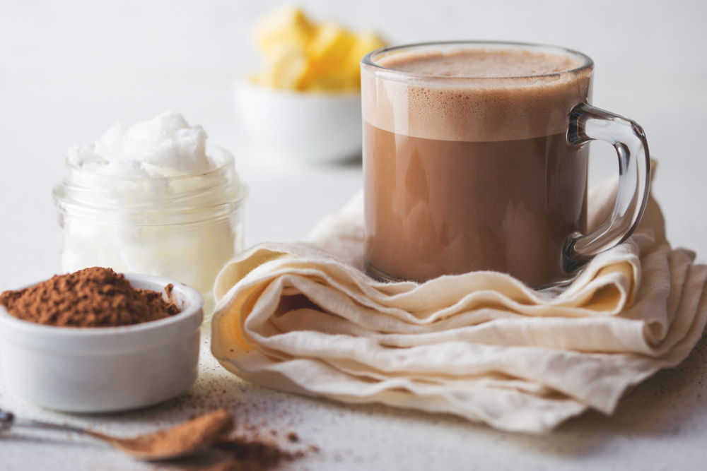 BULLETPROOF CACAO. Ketogenic keto diet hot drink. Cacao blended with coconut oil and butter. Cup of bulletproof cacao and ingredients on white background.