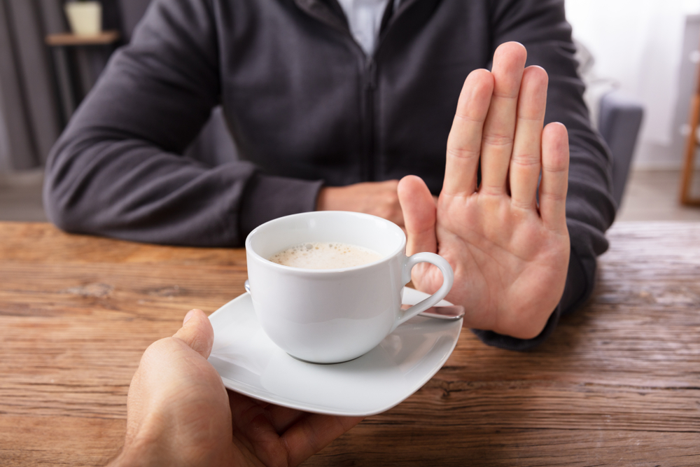 Close-up Of A Man's Hand Refusing Cup Of Coffee Offered By Person Over Wooden Desk
