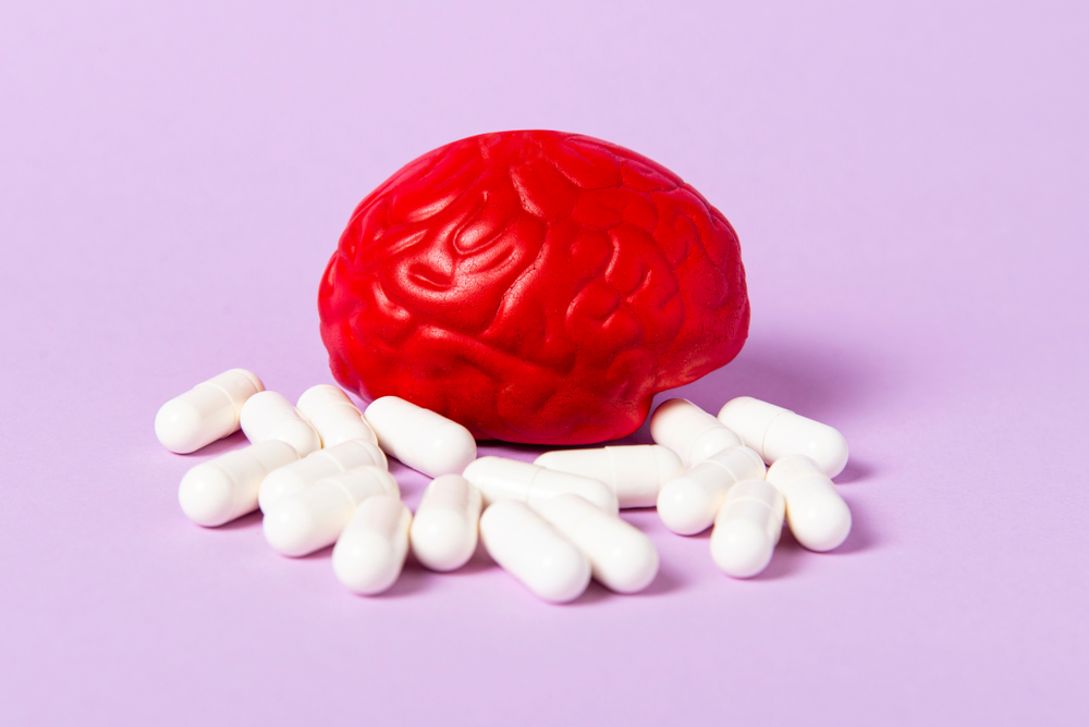 Red brain on a pink background with white pills. Some pills for the brain. Symbolic for drugs, psychopharmaceuticals, nootropics and other drugs. The medicine. Brain treatment