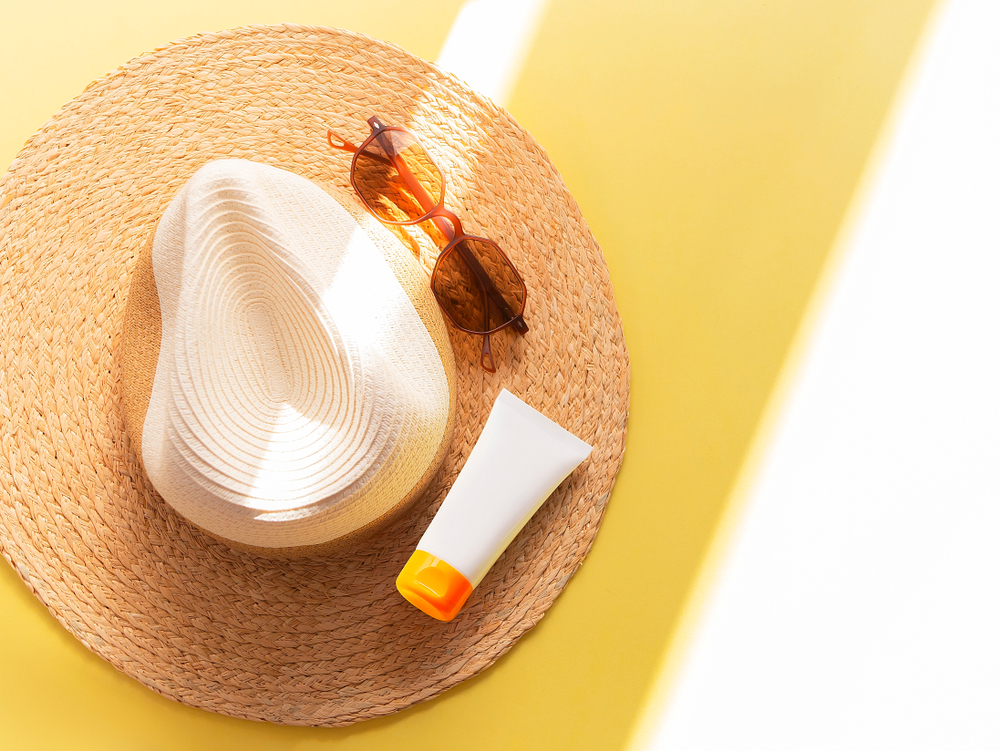 Sunprotection objects. Straw woman's hat with sun glasses and protection cream spf 30 top view on bright yellow background. Beach accessories. Summer Travel Vacation Concept. Sale kit. Copy space.
