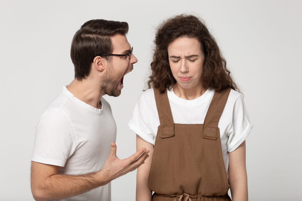 Young unhappy couple isolated on grey studio background, mad angry guy open mouth screaming at girlfriend, girl standing desperate listening aloud yelling feels weak abused crying unable to fight back