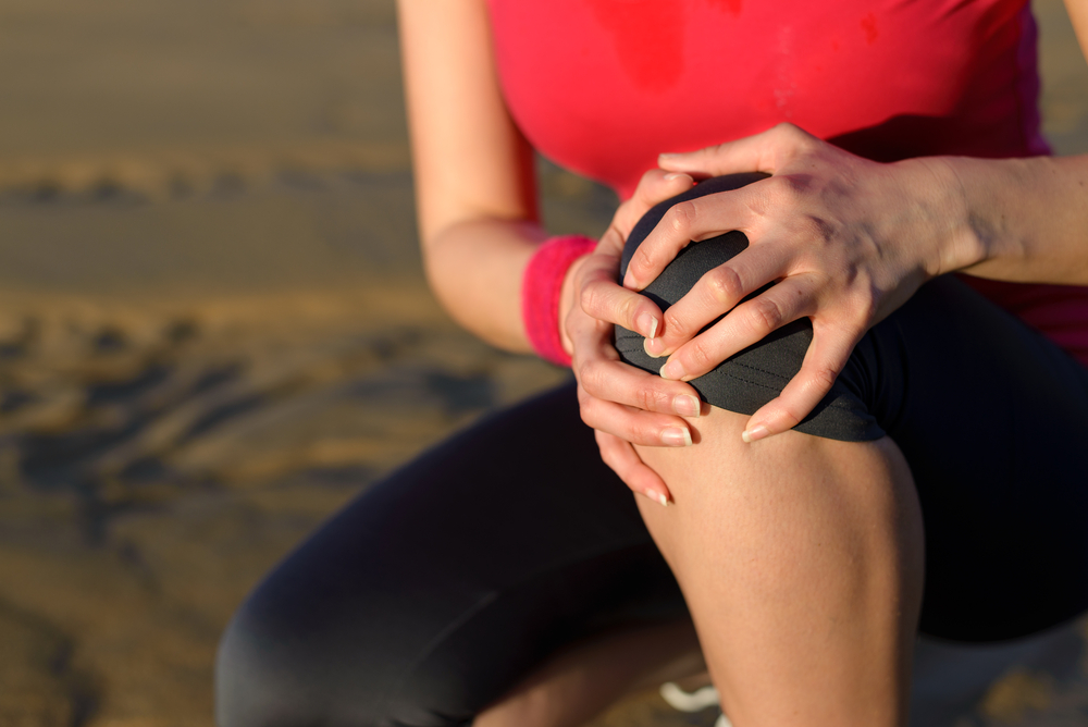 Runner sport knee injury. Woman in pain while running in beach. 