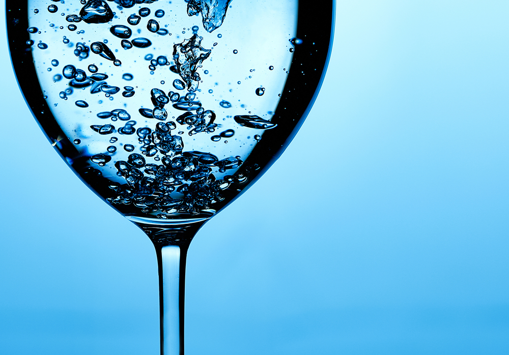 Pouring water into a glass against light blue background. fresh water a glass with bubbles blue background