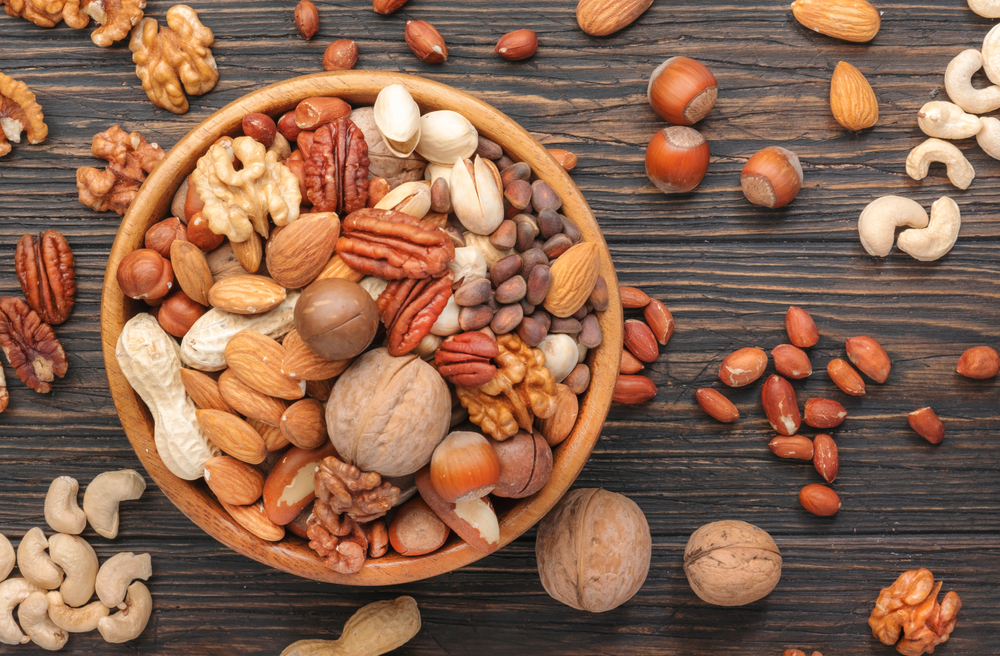 Assortment of nuts in bowls. Cashews, hazelnuts, walnuts, pistachios, pecans, pine nuts, peanuts, macadamia, almonds, brazil nuts. Food mix on wooden background, top view, copy space