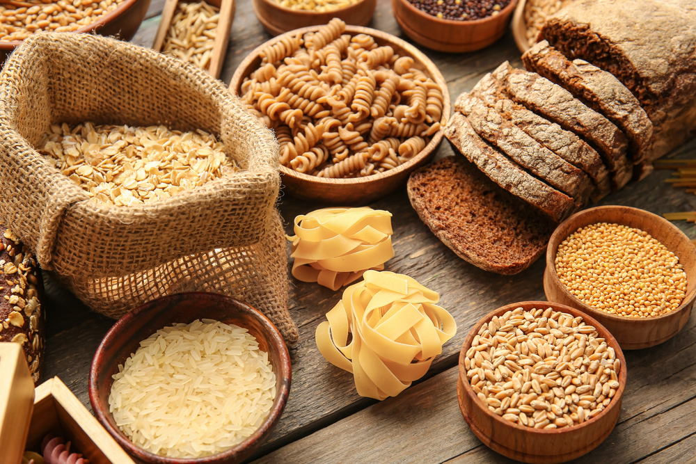 Different cereals, raw pasta and bread on wooden background, closeup
