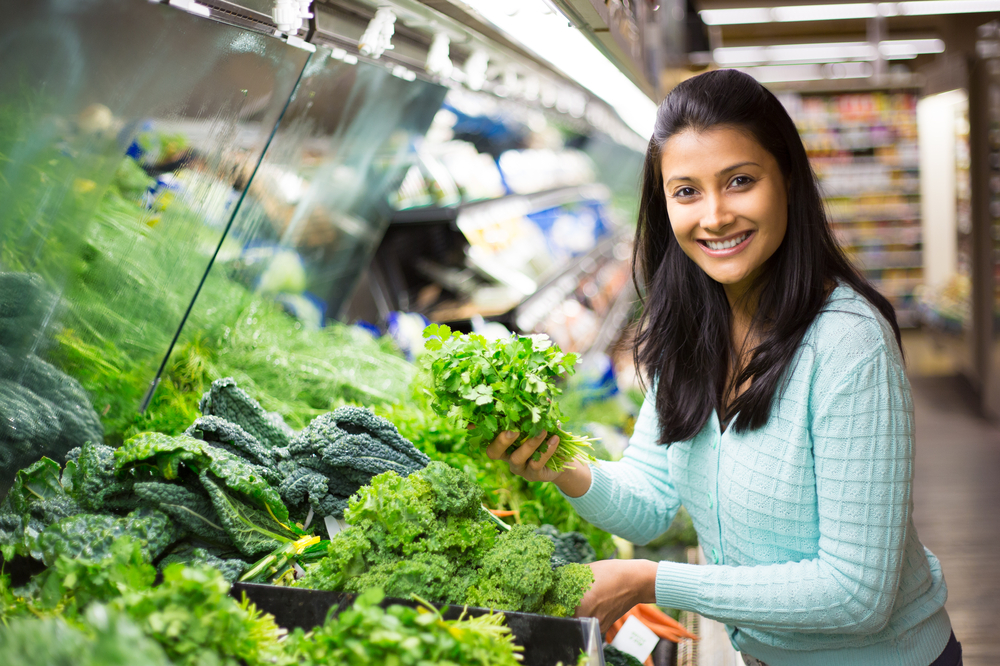 Closeup portrait, beautiful, pretty young woman in sweater picking up, choosing green leafy vegetables in grocery store