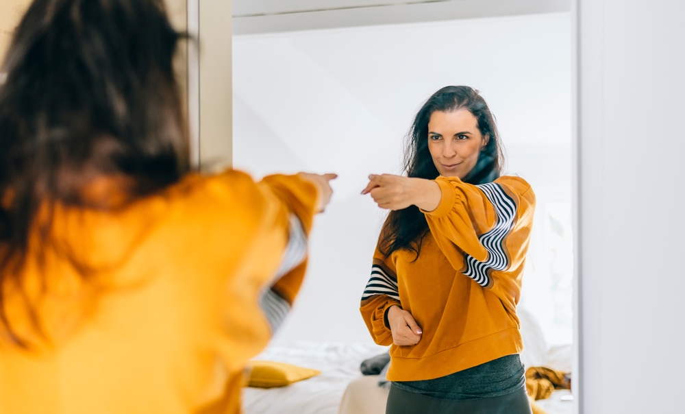 Self confident single woman pointing finger at her reflection in mirror, dancing and felling good. Independent person with high self esteem talks positive and I can do it motivation.
