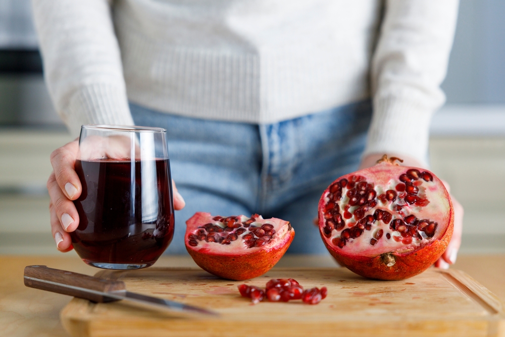 Young woman peeling a pomegranate and holding a glass of pomegranate juice
