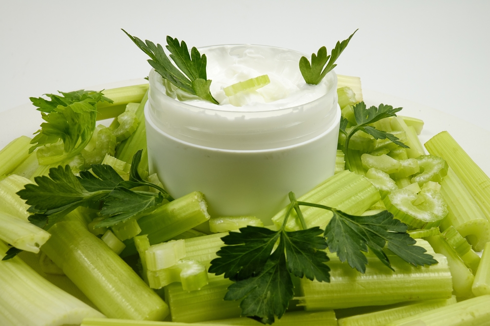 Jar of a natural celery-infused cream, and fresh celery stalks, background