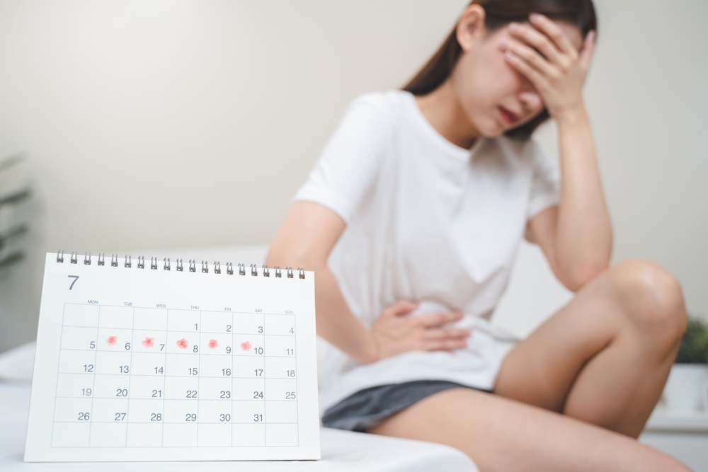 Monthly menstruation symptom period concept. Close up calendar marking on menstruation period day and woman have stomach pain as background.

