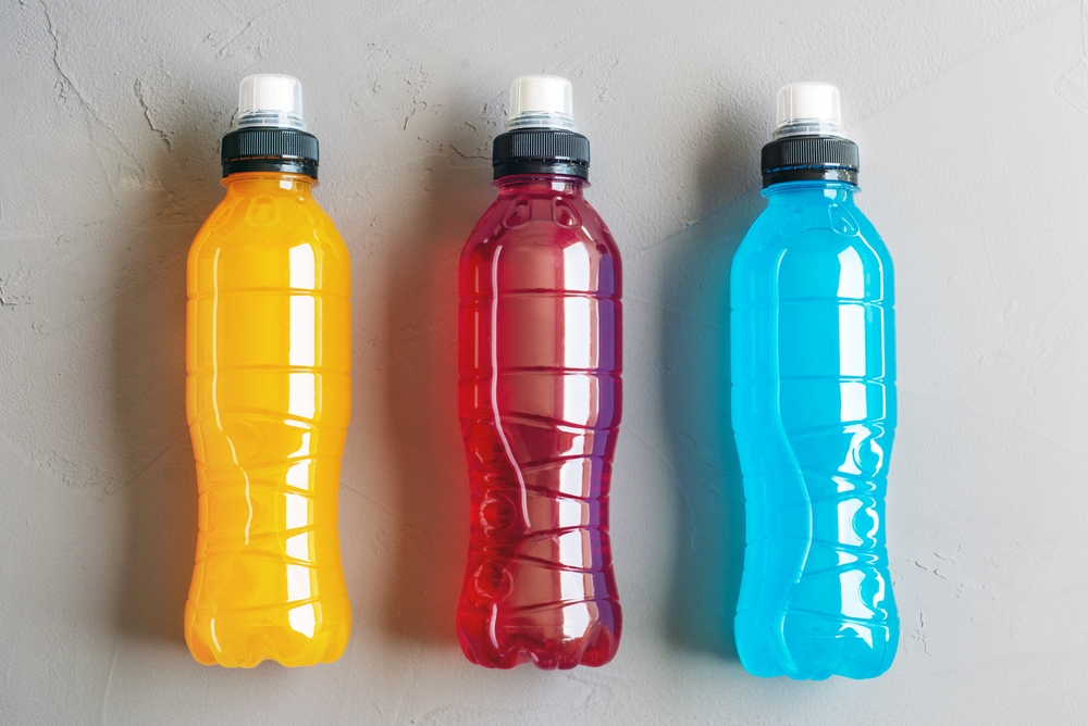 Flat lay shot of three bottles of orange, red and blue isotonic drink on a grey concrete background
