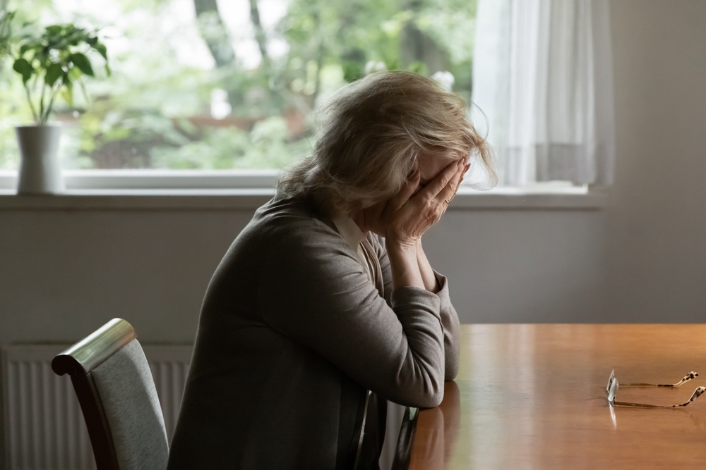 Unhappy old Caucasian woman sit at table at home cry feeling depressed sad suffer from life or health problems. Upset lonely mature female distressed with loneliness solitude, mourn yearn at home.
