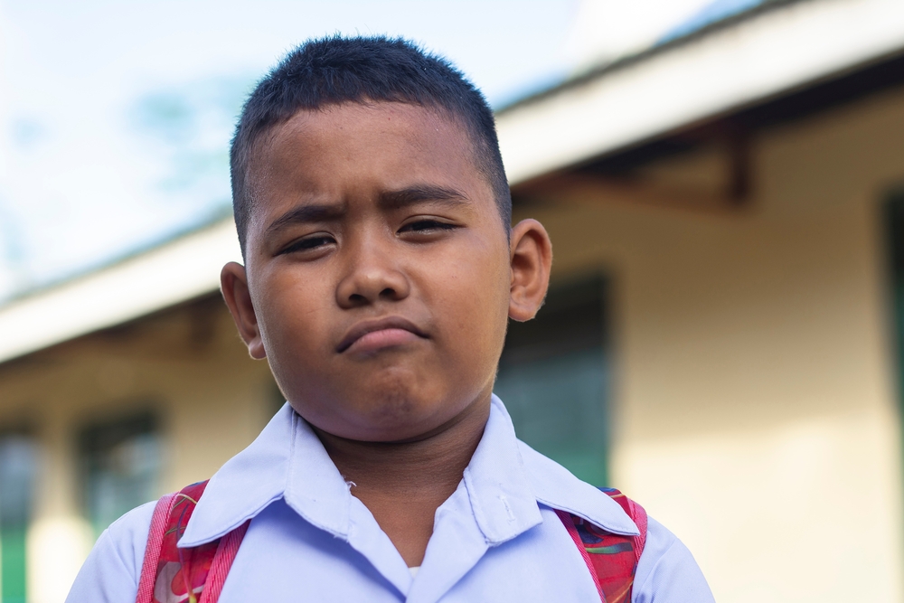 A young asian boy sulking while looking at camera. Throwing a mild tantrum after being scolded. A rural elementary student wearing his school uniform.
