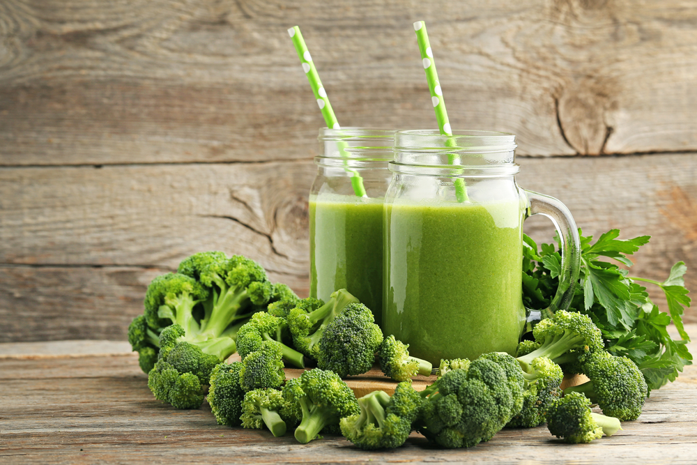 Bottles of juice with broccoli and parsley on grey wooden table
