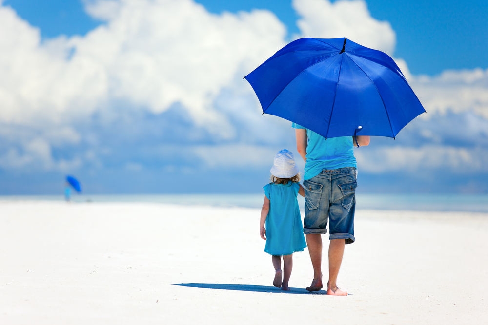 Father and daughter at beach with umbrella to hide from sun
