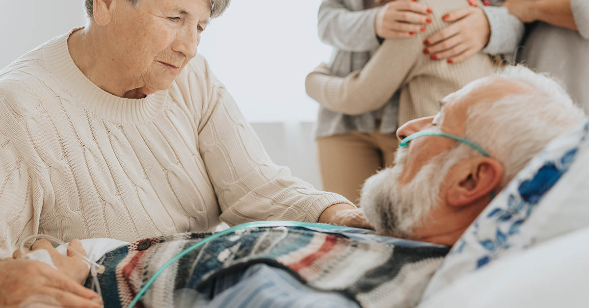 elderly woman comforting man in hospital bed