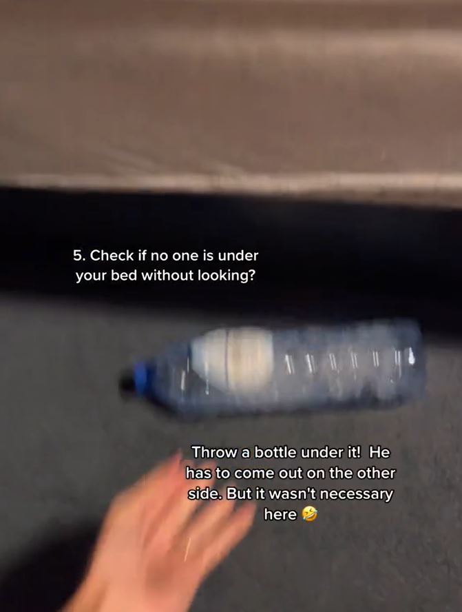 A captioned picture of a hand throwing a bottle under a hotel bed. Carpet and bed in the background. 