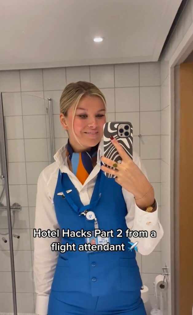 A flight attendant posing in front of a mirror. Bathroom wall and toilet paper in the background. 