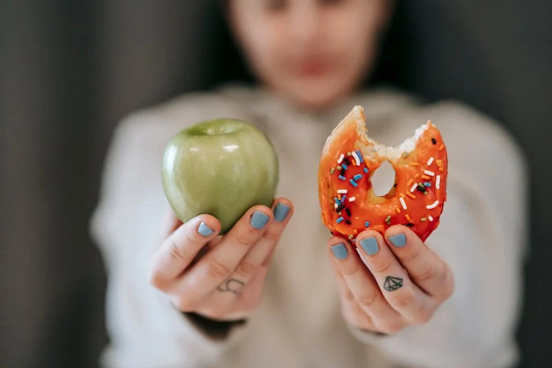 Woman holding an apple beside a donut