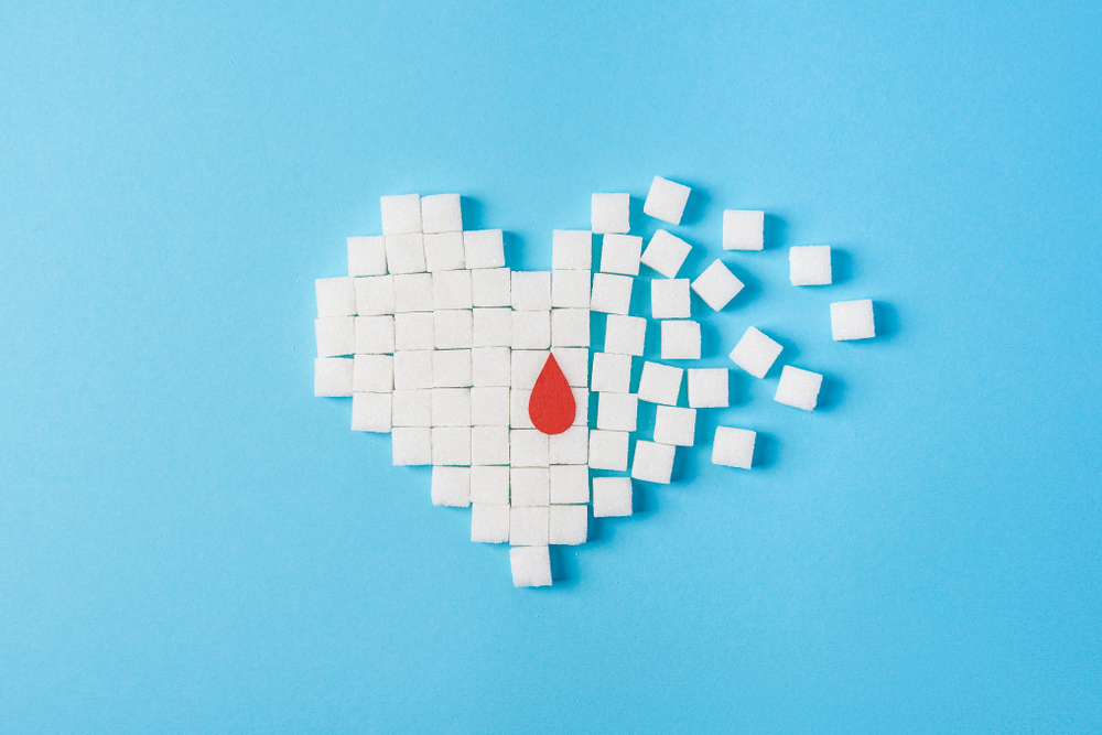 the drop of blood on broken heart made of pure white cubes of sugar isolated on blue background, World diabetes day, November 14