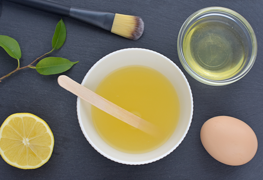 Acne skin treatment, homemade facial mask with egg white and lemon juice, flat lay with ingredients on black background.