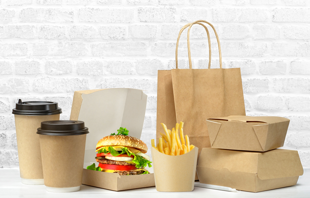 Fast food eco packaging big lunch set of tasty hamburger, french fries, paper coffee cups, brown paper bag and box on the table on white brick wall background